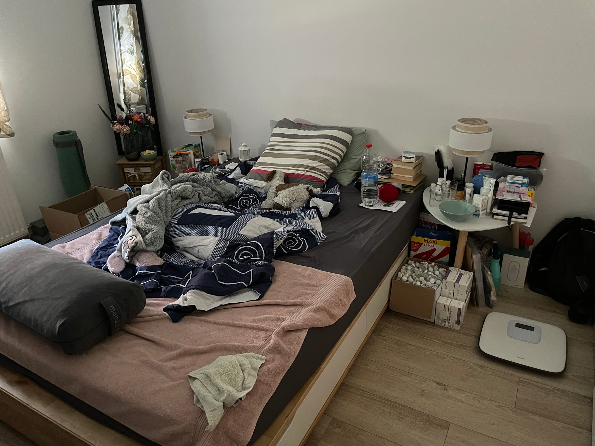 View of my messy bedroom with a lot of things around the bed, like towels, medication, etc.